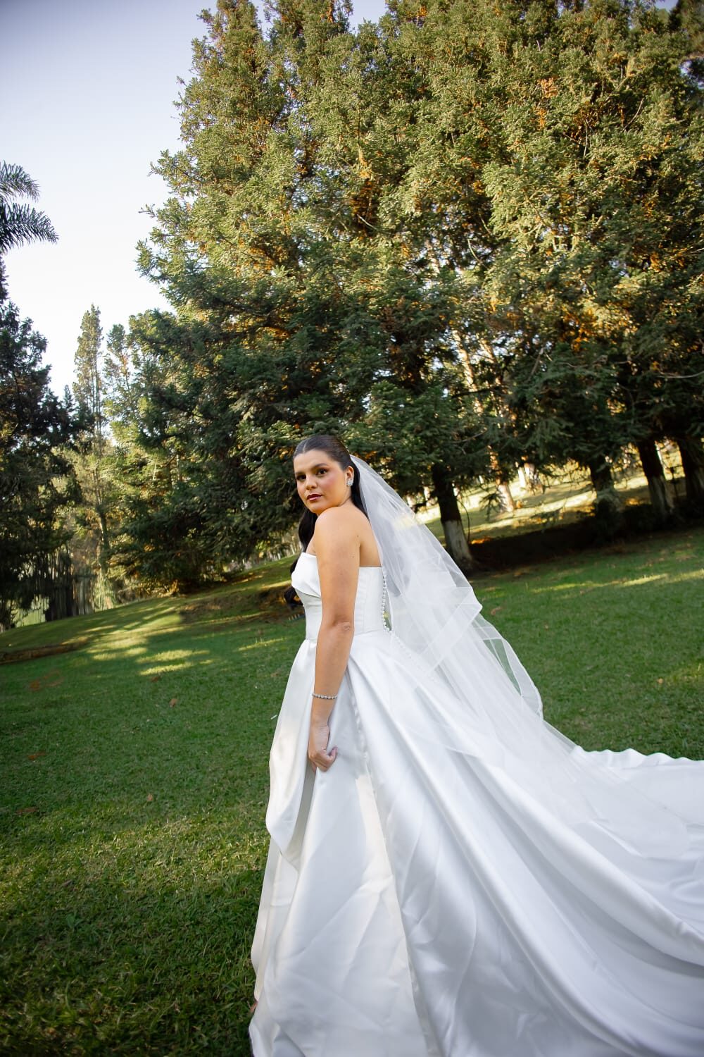 Noiva de costas no jardim, véu ao vento
